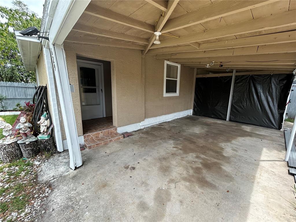 A covered carport features a concrete floor, a tan stucco wall, and a side entrance — 629 HOLMES AVENUE, DAYTONA BEACH, FL