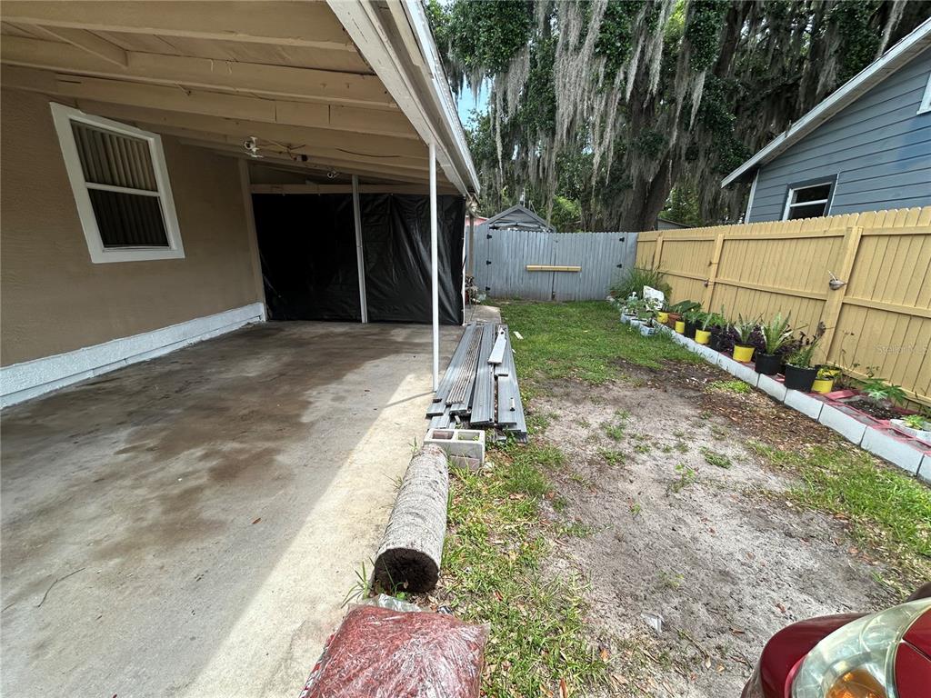 A concrete carport sits beside a small yard with a wooden fence and potted plants — 629 HOLMES AVENUE, DAYTONA BEACH, FL