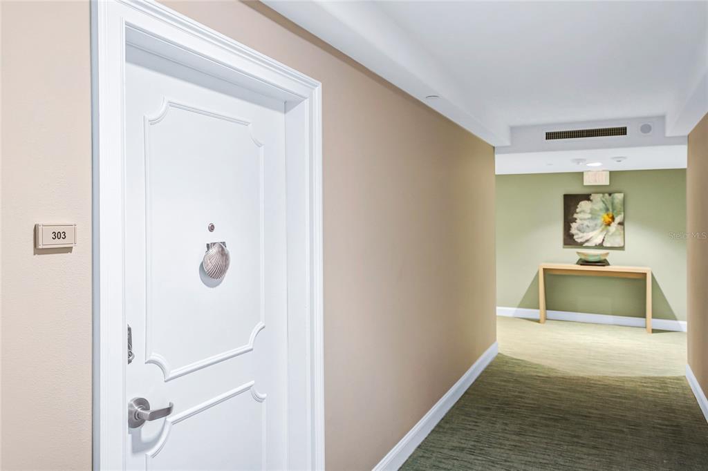 A white door with a seashell knocker leads to a hallway with a console table — 1212 BENJAMIN FRANKLIN DRIVE UNIT 303, SARASOTA, FL