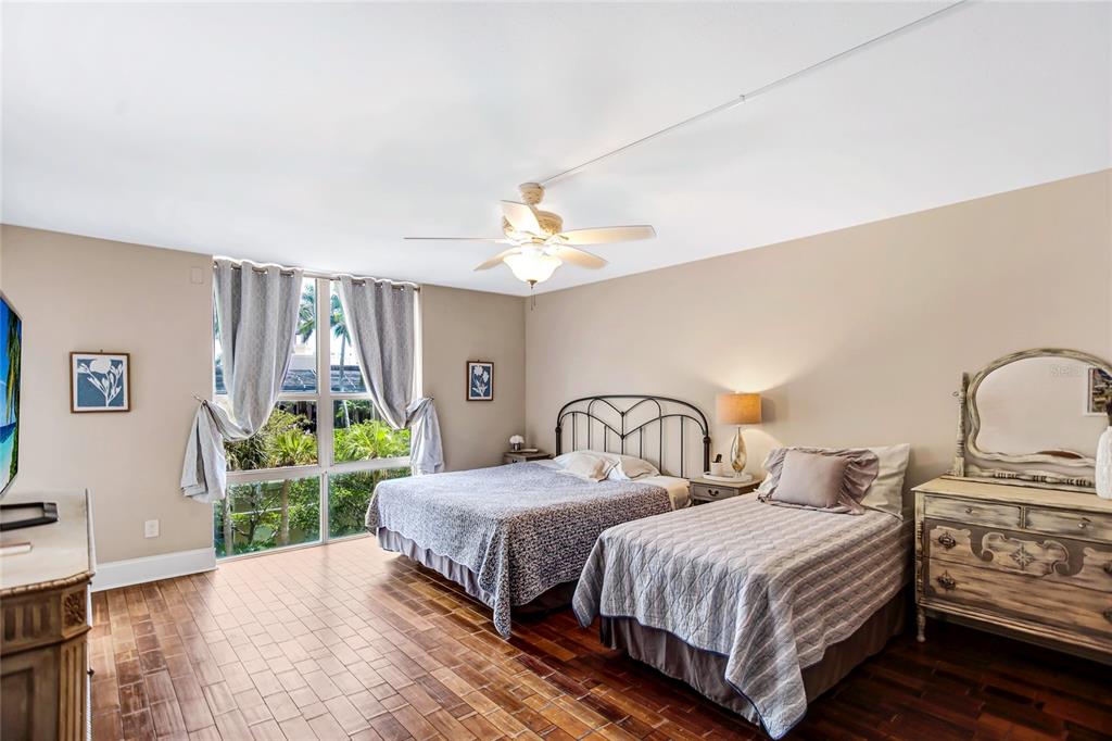 A bedroom features two beds, wood flooring, a ceiling fan, and large windows with garden views — 1212 BENJAMIN FRANKLIN DRIVE UNIT 303, SARASOTA, FL