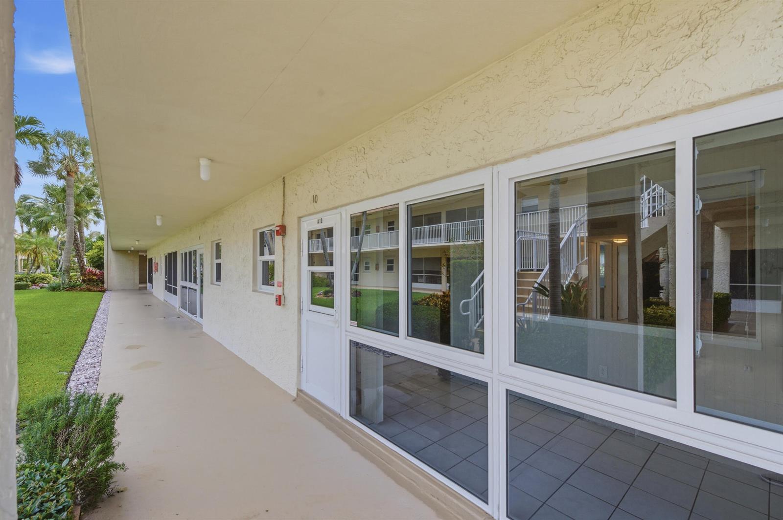 A covered exterior walkway leads past a white door and large windows of a building — 600 Snug Harbor Drive # A10, Boynton Beach FL 33435, BOYNTON BEACH, FL