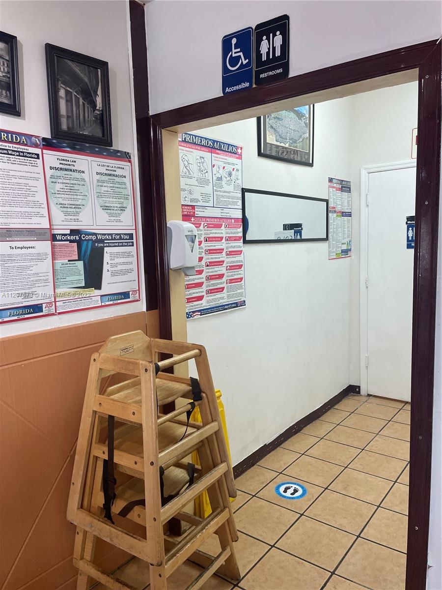 A wooden high chair stands in a hallway leading to a restroom with tiled floors — 8726 NW 26th St, Doral FL 33172, DORAL, FL