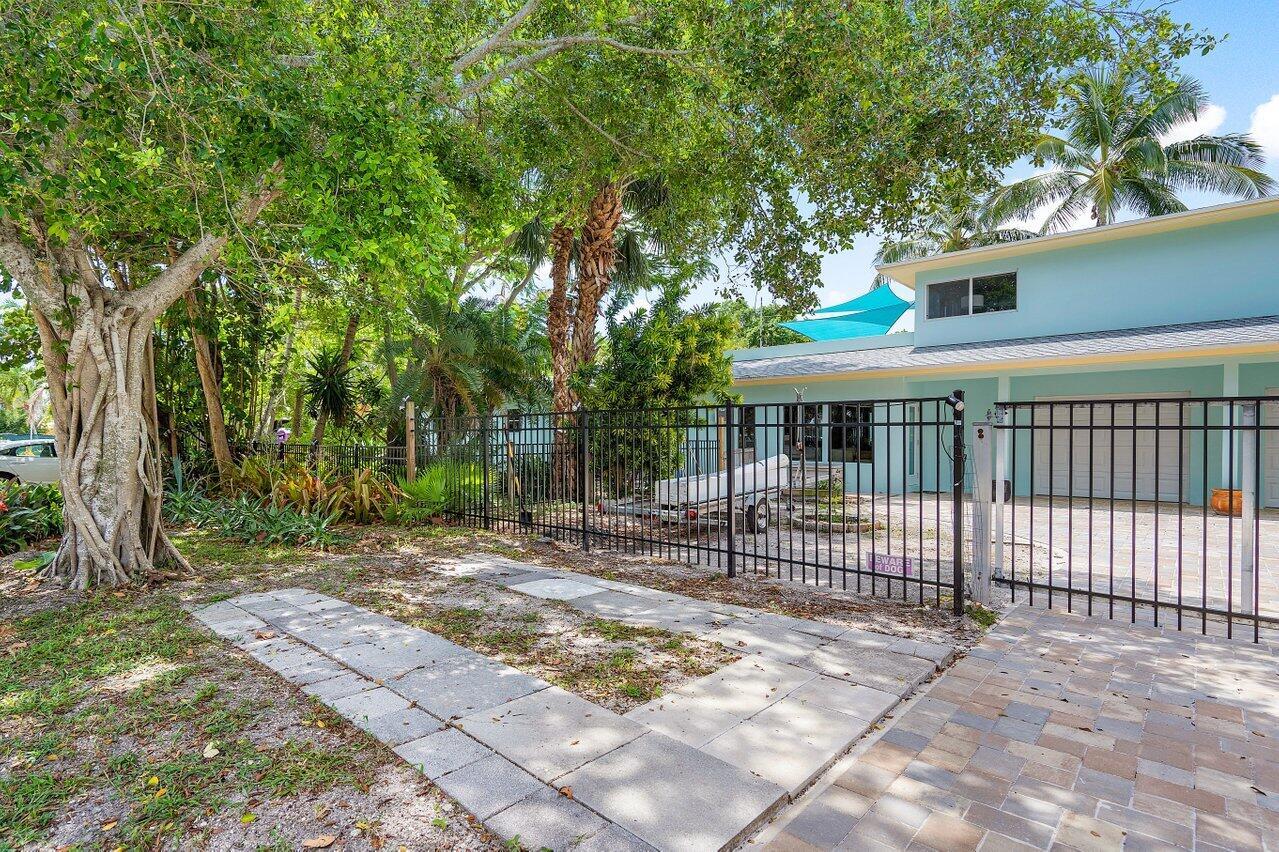 A fenced yard with a paved driveway, mature trees, and a light blue house exterior — 300 SE 7th Avenue, Delray Beach FL 33483, DELRAY BEACH, FL
