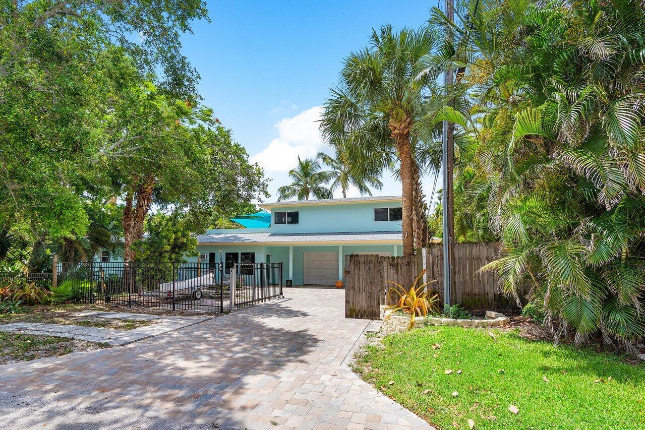 A light blue two-story house features a paved driveway, a wooden fence, and palm trees — 300 SE 7th Avenue, Delray Beach FL 33483, DELRAY BEACH, FL