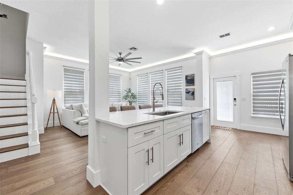 A modern kitchen features white cabinetry, a marble-topped island with bar stools, and wood flooring — 185 LONGVIEW AVENUE, KISSIMMEE, FL