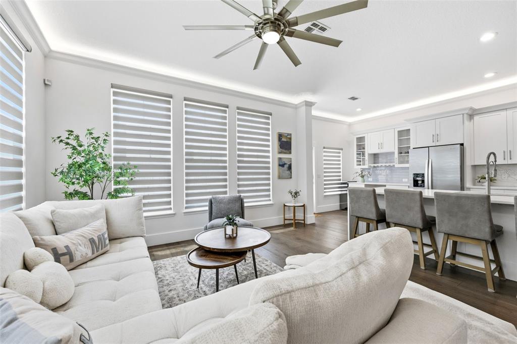 A bright open-concept living room and kitchen featuring white cabinetry, wood floors, and neutral furniture — 185 LONGVIEW AVENUE, KISSIMMEE, FL