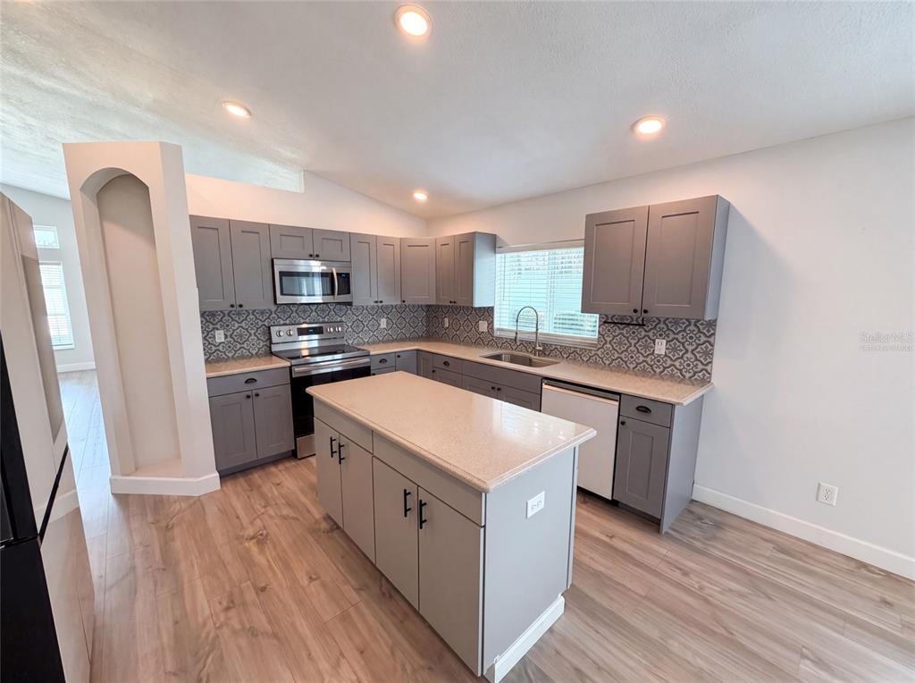 A kitchen features gray cabinets, a central island, light countertops, and a patterned tile backsplash — 3800 SEMINOLE DRIVE, ORLANDO, FL
