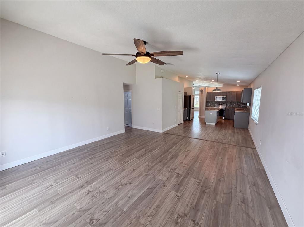 An open-concept living area features wood-look flooring, a ceiling fan, and an adjacent kitchen — 3800 SEMINOLE DRIVE, ORLANDO, FL