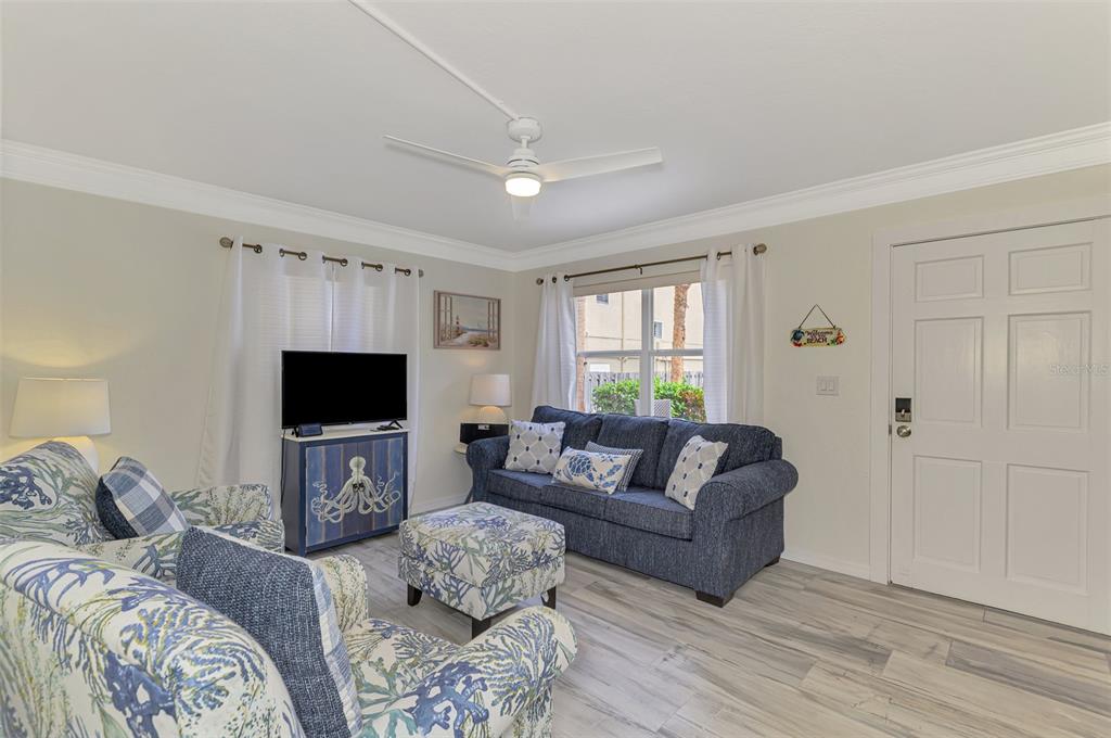 A living room features a blue sofa, patterned armchair, television, and light wood-look flooring — 446 CANAL ROAD UNIT 5, SARASOTA, FL