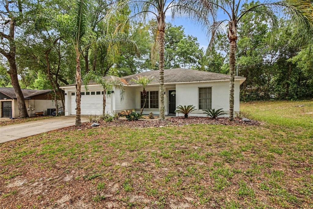 A single-story white house with a garage and palm trees sits on a grassy lot — 1166 15TH STREET, ORANGE CITY, FL