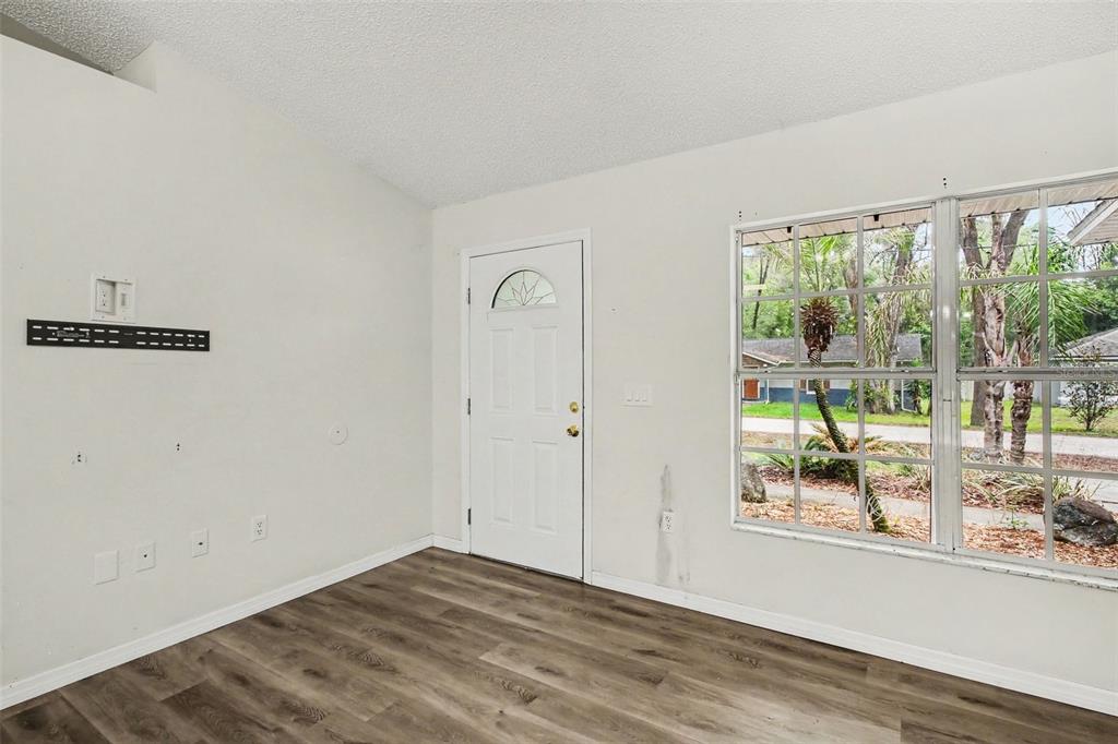An empty room features wood-look flooring, a white front door, and a large window — 1166 15TH STREET, ORANGE CITY, FL
