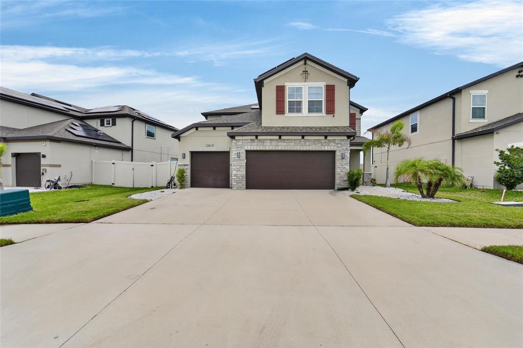 A two-story suburban house features a three-car garage, stone accents, and a concrete driveway — 13519 PALMERA VISTA DRIVE, RIVERVIEW, FL
