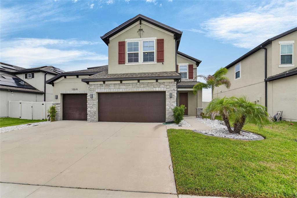 A two-story suburban house with a three-car garage, stone facade, and a small front lawn — 13519 PALMERA VISTA DRIVE, RIVERVIEW, FL