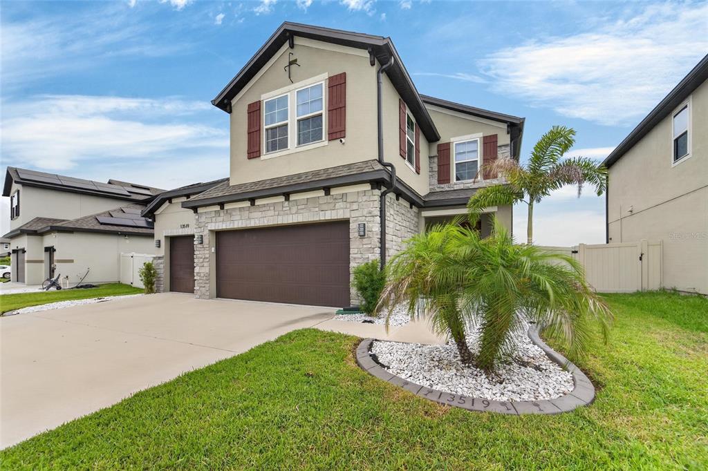 A two-story suburban house features a stone facade, a three-car garage, and a palm tree — 13519 PALMERA VISTA DRIVE, RIVERVIEW, FL