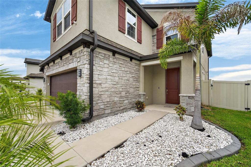 A two-story house exterior features a stone facade, a brown garage door, and a palm tree — 13519 PALMERA VISTA DRIVE, RIVERVIEW, FL