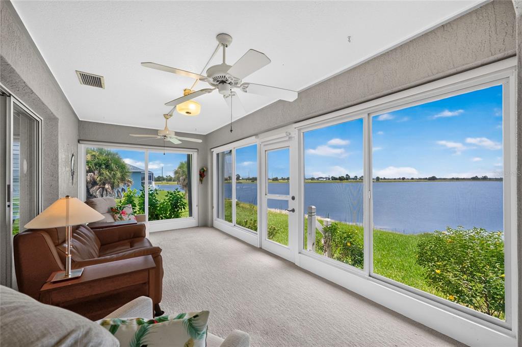 A sunroom with carpeted floors, ceiling fans, and large windows overlooking a lake — 31 MEADOWLARK LANE, PLACIDA, FL