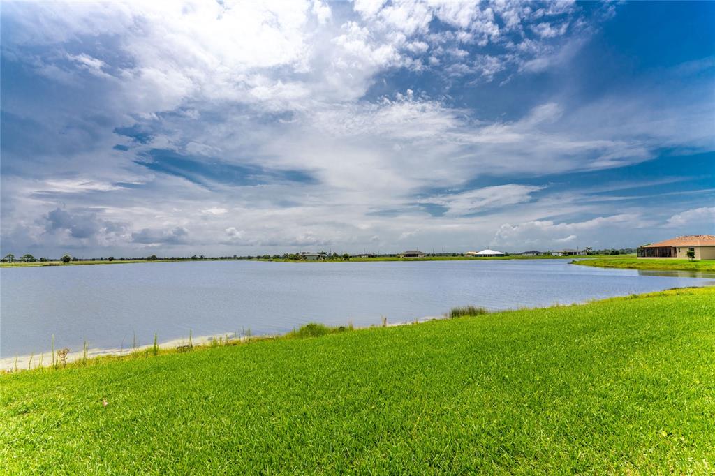 A grassy lawn overlooks a large pond with houses visible in the distance under clouds — 31 MEADOWLARK LANE, PLACIDA, FL