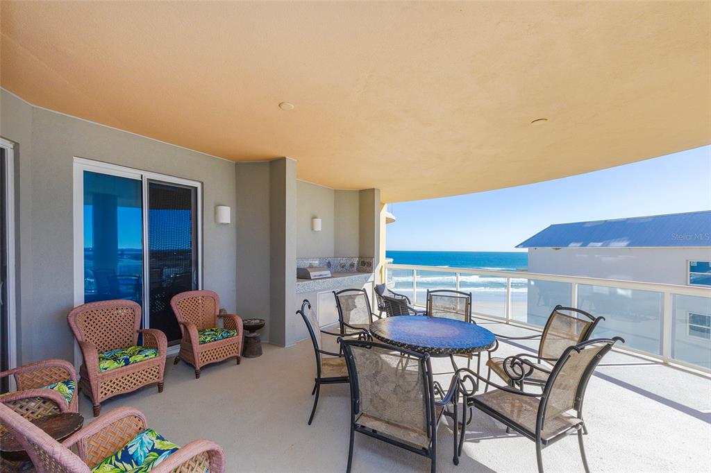 A covered balcony features wicker chairs, a dining set, a built-in grill, and ocean views — 3703 S ATLANTIC AVENUE UNIT 505, DAYTONA BEACH SHORES, FL