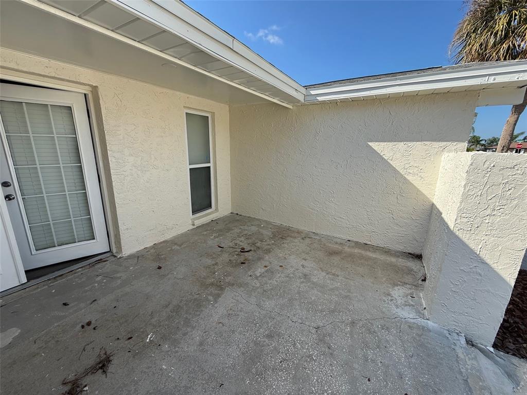 A concrete patio sits outside a white door and window against a textured stucco wall — 6104 SEABREEZE DRIVE, PORT RICHEY, FL
