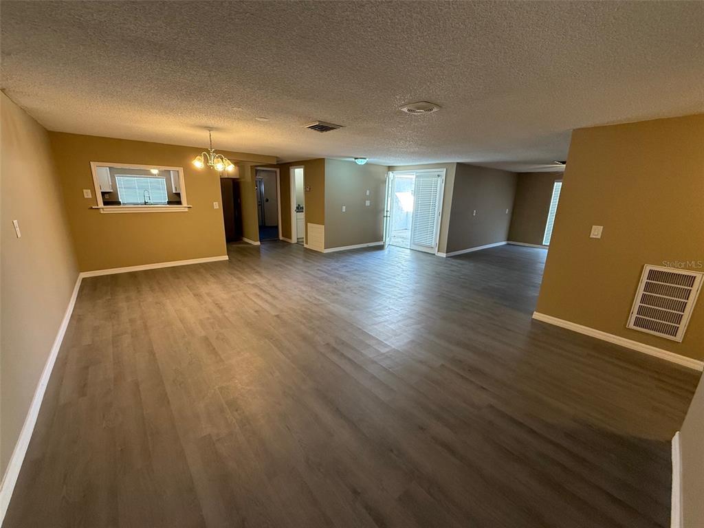 An open-concept living area features light brown walls, gray wood-look flooring, and a sliding door — 6104 SEABREEZE DRIVE, PORT RICHEY, FL