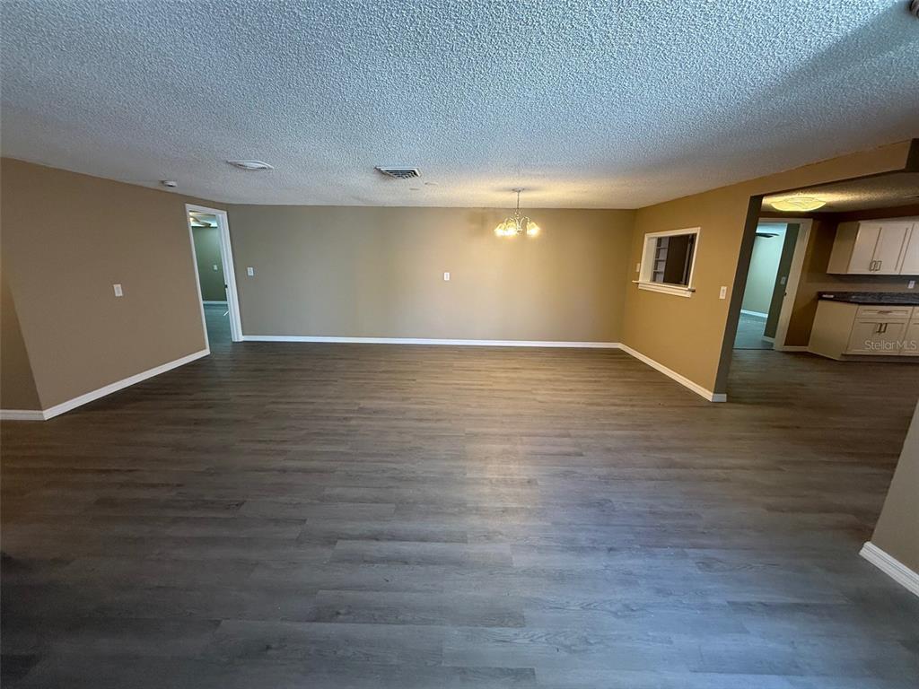 A spacious room with wood-look flooring, beige walls, a popcorn ceiling, and a dining chandelier — 6104 SEABREEZE DRIVE, PORT RICHEY, FL