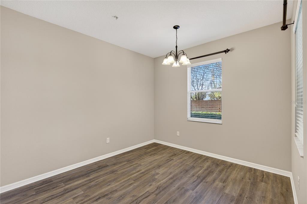 An empty room with beige walls, wood-look flooring, a chandelier, and a window with blinds — 1519 PRIORY CIRCLE, WINTER GARDEN, FL