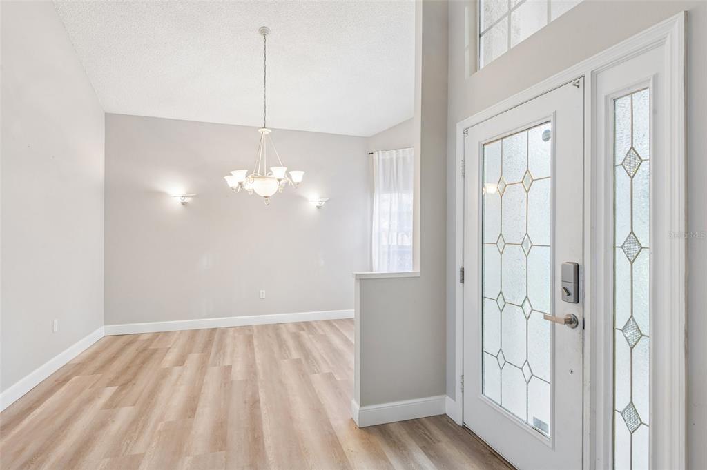 A dining area with wood-look flooring, a chandelier, and wall sconces near a front door — 586 KINGSMILL COURT, OLDSMAR, FL