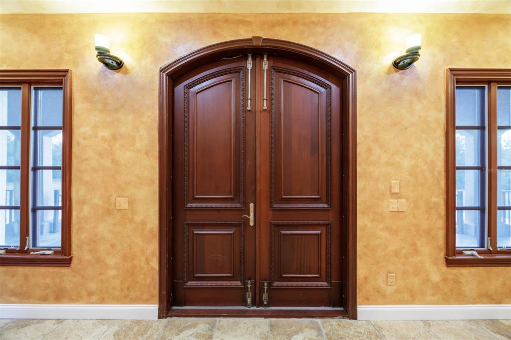 A pair of arched wooden double doors sits between two windows on a textured wall — 18910 NW 78TH AVENUE, ALACHUA, FL