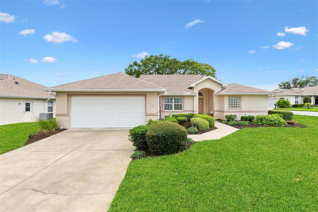 A single-story house with a beige stucco exterior, a two-car garage, and a landscaped lawn — 11736 SE 176TH PLACE ROAD, SUMMERFIELD, FL