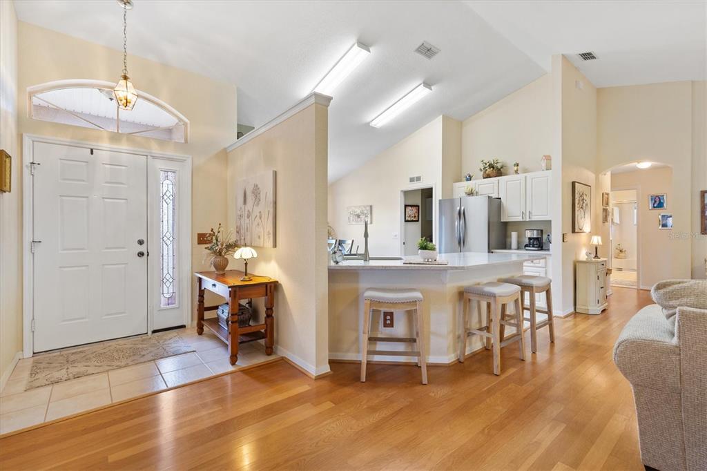 An entryway with wood floors leads to an open kitchen featuring a breakfast bar — 11736 SE 176TH PLACE ROAD, SUMMERFIELD, FL