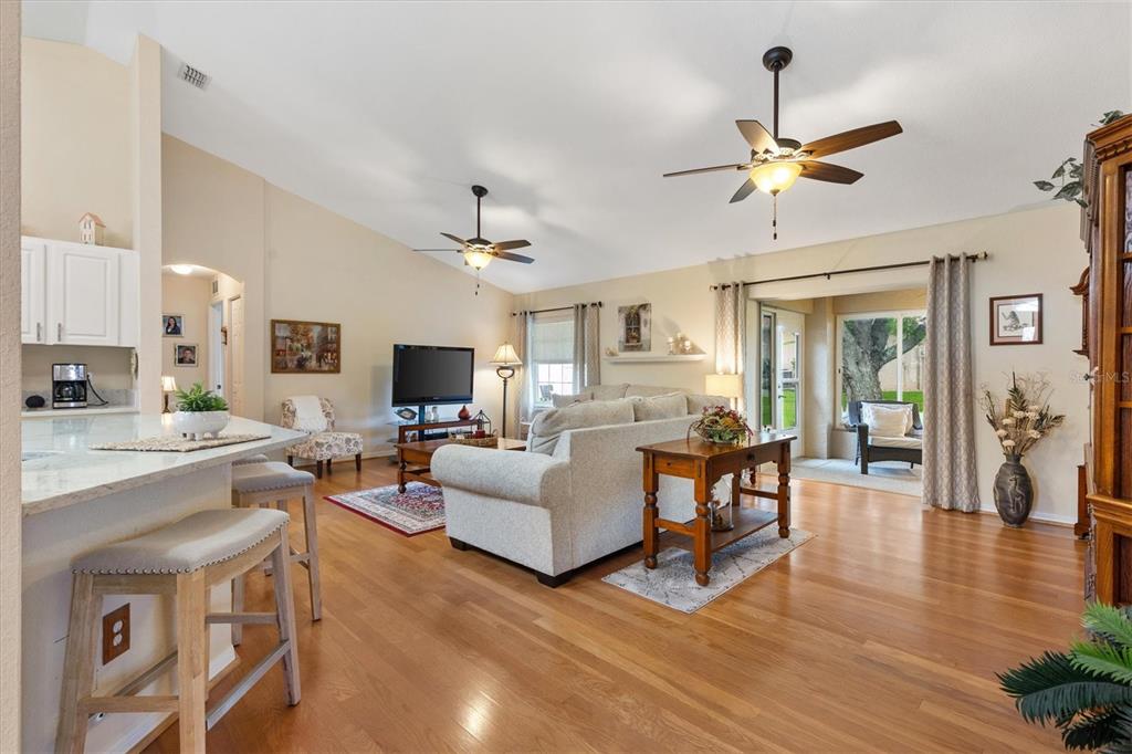 A living room with hardwood floors, a light-colored sofa, and two ceiling fans — 11736 SE 176TH PLACE ROAD, SUMMERFIELD, FL