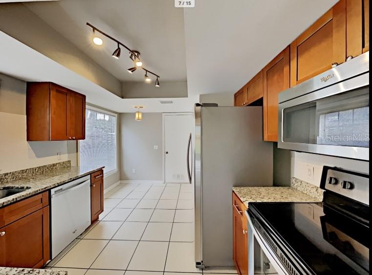 A kitchen features wood cabinets, stainless steel appliances, tile flooring, and a track lighting fixture — 1680 PALM LEAF DRIVE, BRANDON, FL