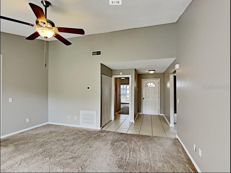 A living room features beige carpeting, a vaulted ceiling with a fan, and a tiled entryway — 1680 PALM LEAF DRIVE, BRANDON, FL