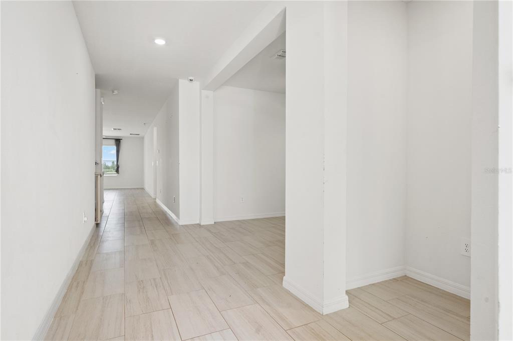 A hallway with light-colored tile flooring leads toward a window in a white-walled interior — 22313 PLEASANT MORNING DRIVE, LAND O LAKES, FL