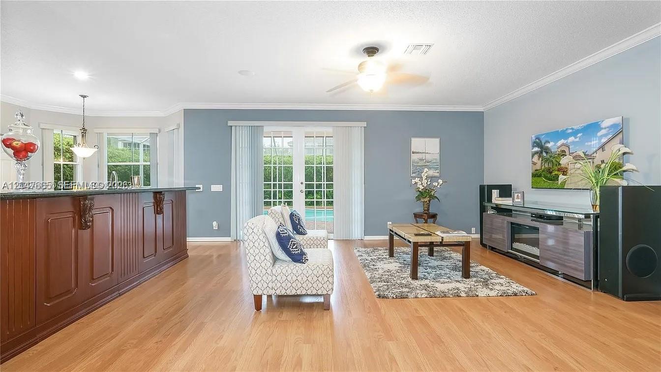 A living room features hardwood floors, a blue accent wall, and a view of a pool — 1714 Royal Grove Way, Weston FL 33327, WESTON, FL