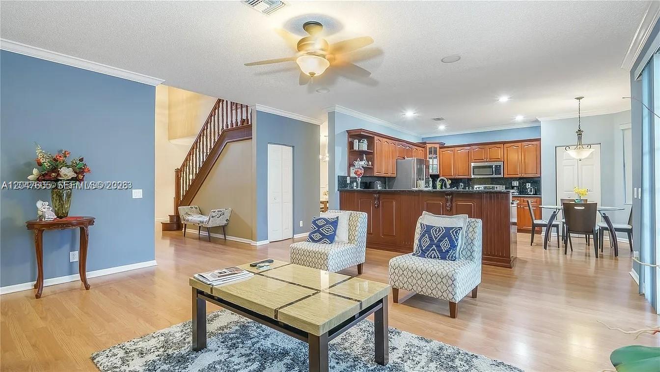 An open-concept living room features light wood floors, blue walls, and a wooden staircase — 1714 Royal Grove Way, Weston FL 33327, WESTON, FL