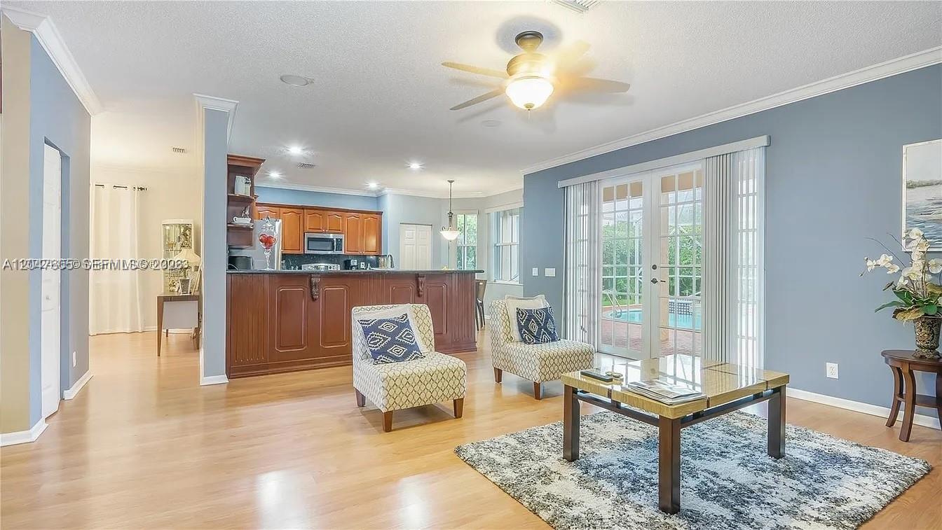 A living room with light wood floors opens to a kitchen with dark wood cabinetry — 1714 Royal Grove Way, Weston FL 33327, WESTON, FL