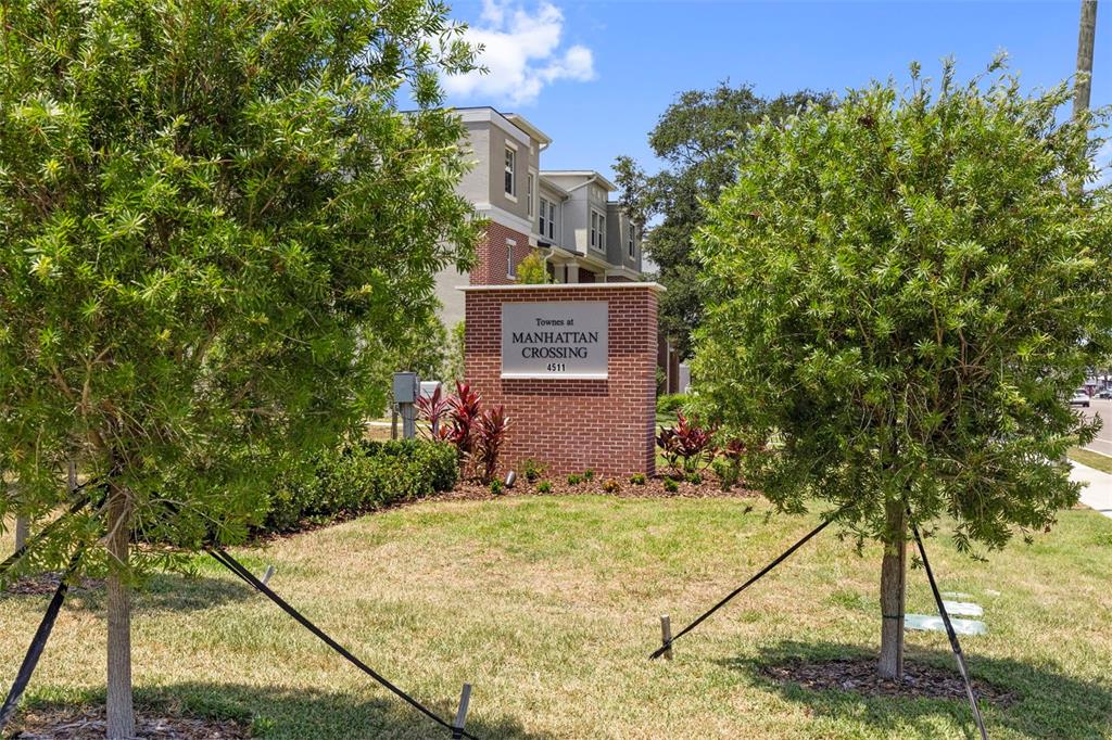 A brick monument sign stands in front of a multi-story residential building and trees — 4511 S MANHATTAN AVENUE UNIT 17, TAMPA, FL