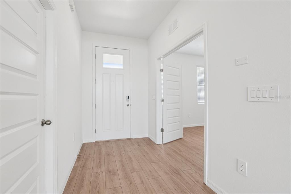 An entryway with wood-look flooring, a white front door, and a doorway leading to another room — 5392 CLOUDBERRY, LAKELAND, FL