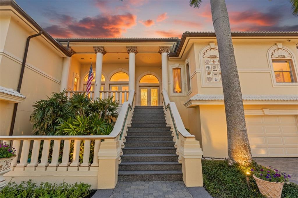 A grand staircase leads to the elevated entrance of a yellow stucco home with columns — 964 MONTE CRISTO BOULEVARD, TIERRA VERDE, FL