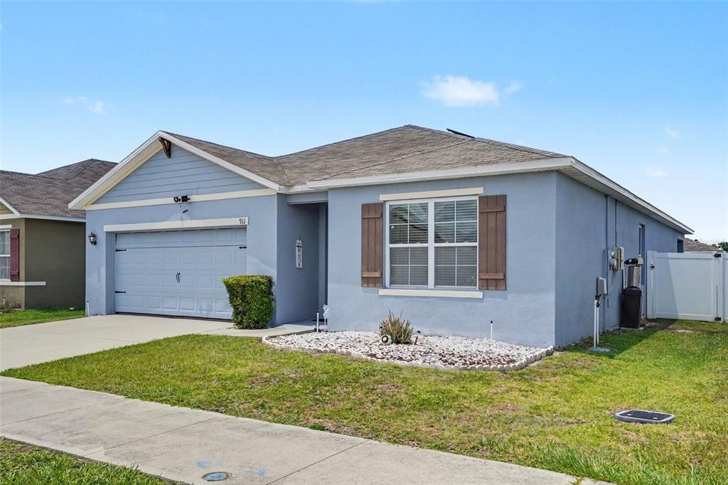 A light blue single-story house with a two-car garage and a front yard — 911 WATERVILLE DR, AUBURNDALE, FL