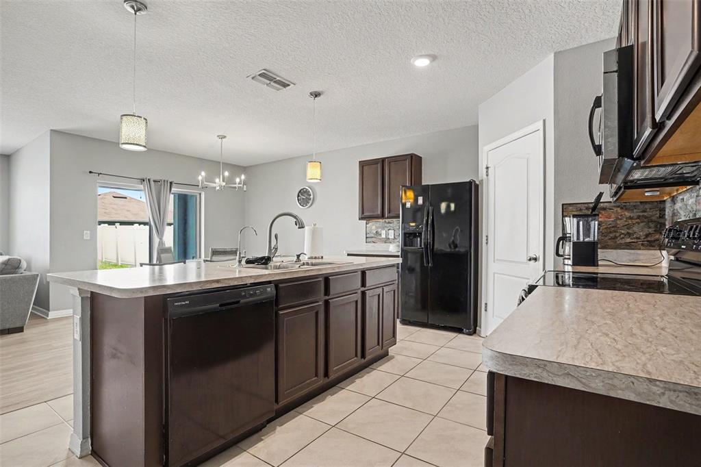 A kitchen features dark wood cabinets, a large island with a sink, and tile flooring — 911 WATERVILLE DR, AUBURNDALE, FL