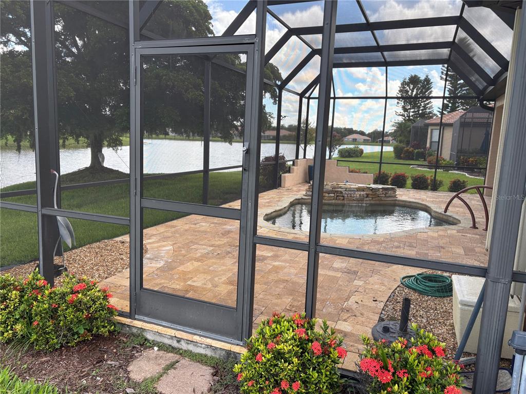 A screened-in patio features a small pool with a stone water feature overlooking a lake — 8053 STIRLING FALLS CIRCLE, SARASOTA, FL