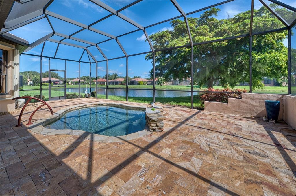 A screened-in patio features a stone-accented spa, paver flooring, and a view of a lake — 8053 STIRLING FALLS CIRCLE, SARASOTA, FL