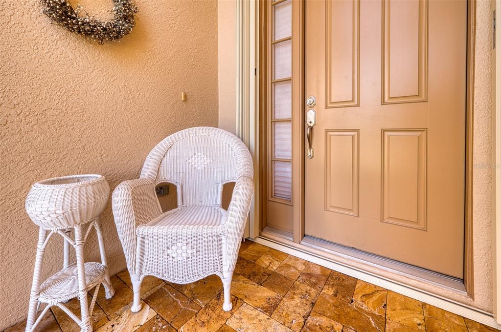 A white wicker chair and small table sit on a tiled porch by a door — 8053 STIRLING FALLS CIRCLE, SARASOTA, FL