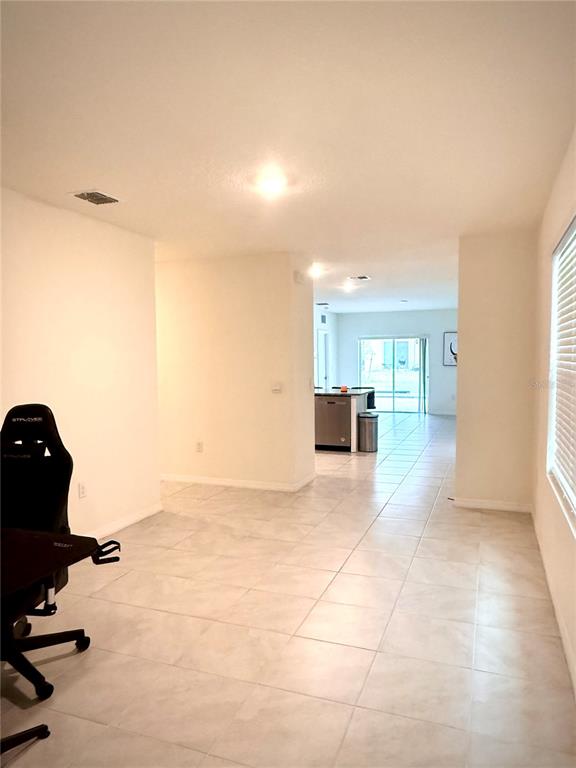 A room with light-colored tile flooring leads toward a kitchen with stainless steel appliances — 2255 TAY WES DRIVE, ST CLOUD, FL