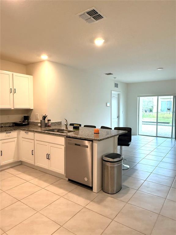 A kitchen with white cabinets, granite countertops, and tile flooring opens to a living area — 2255 TAY WES DRIVE, ST CLOUD, FL