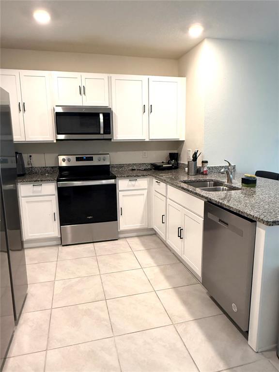 A kitchen features white cabinets, granite countertops, stainless steel appliances, and light-colored tile flooring — 2255 TAY WES DRIVE, ST CLOUD, FL
