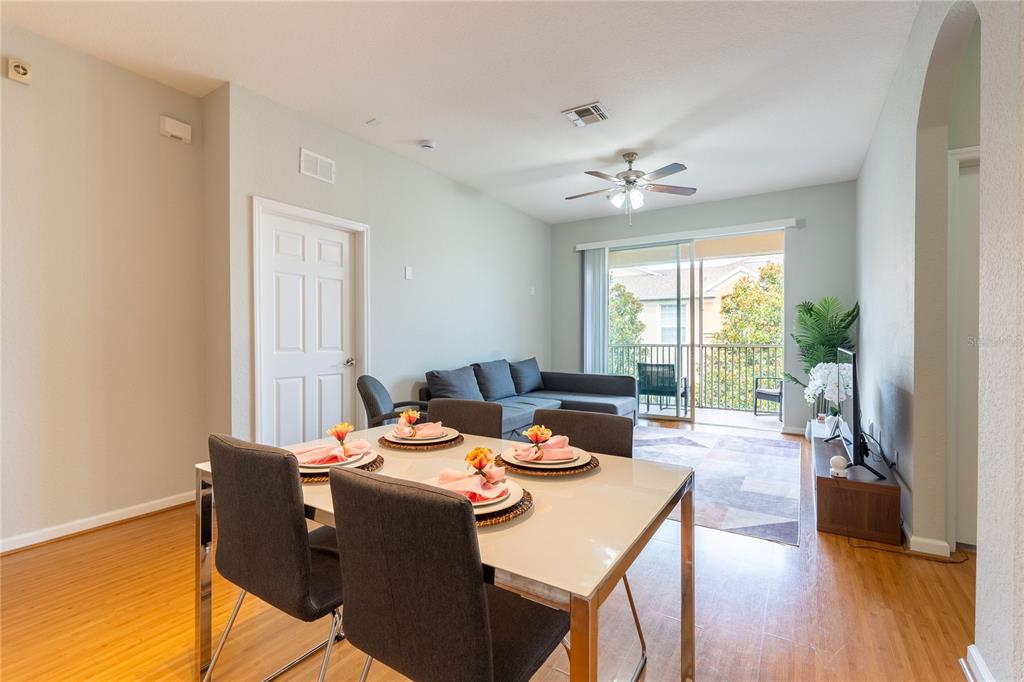 A dining area with a table and chairs opens into a living room with balcony access — 2484 SAN TECLA STREET UNIT 408, ORLANDO, FL