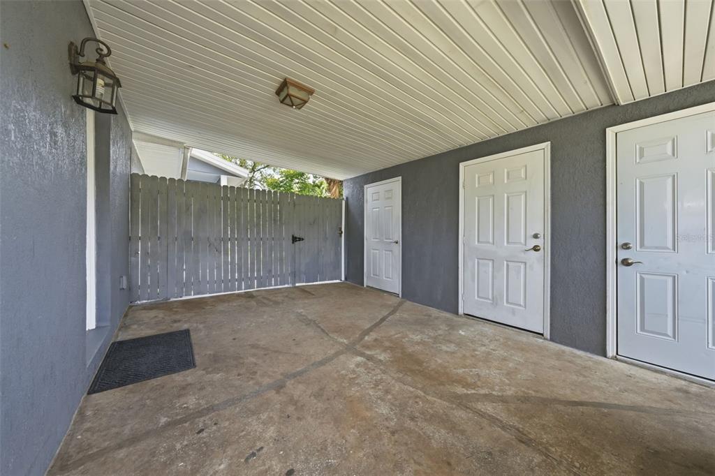 A covered concrete carport features gray walls, a wooden fence, and two white doors — 1311 HILLCREST DRIVE, DAYTONA BEACH, FL